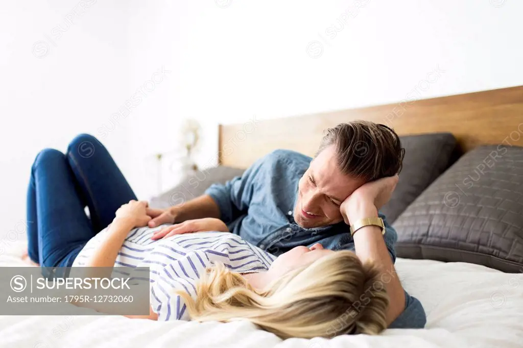 Husband lying down on bed with pregnant wife