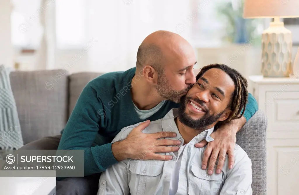 Homosexual couple kissing by sofa in living room