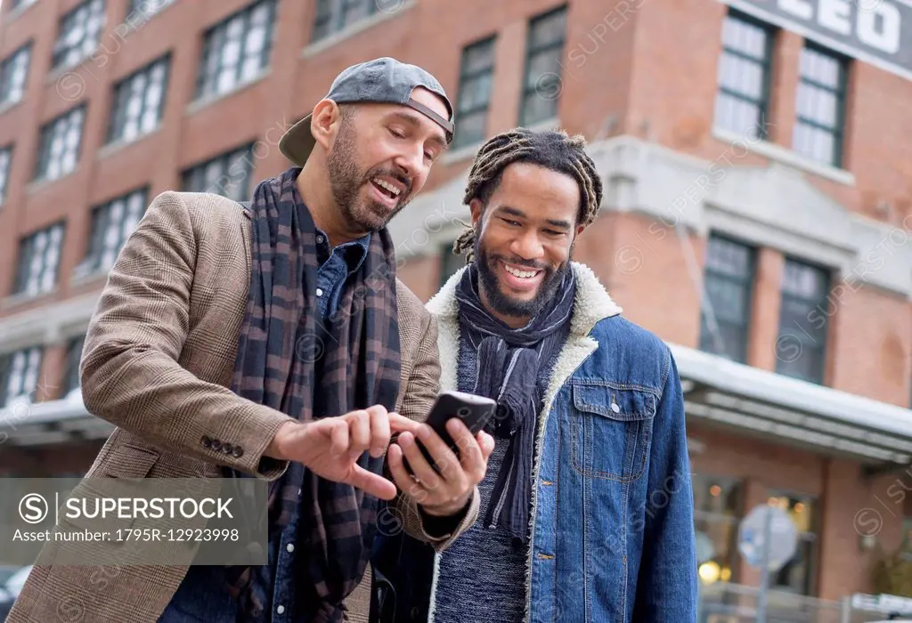 Smiley homosexual couple looking at smart phone in street