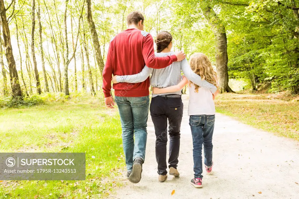 Daughter (8-9) with parents walking in park, rear view