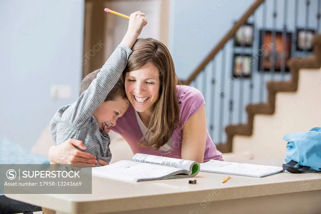Smiling mother hugging son (6-7) doing homework