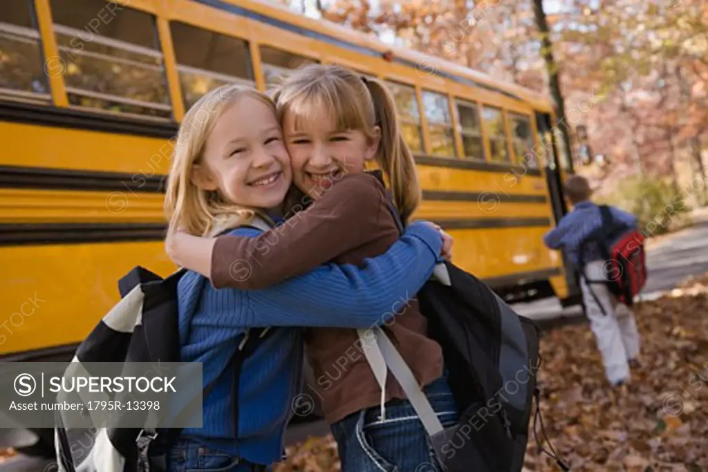 Girls hugging in front of school bus