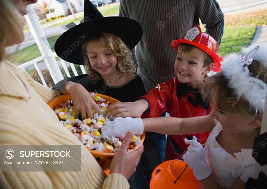 Children in Halloween costumes reaching into bowl of candy