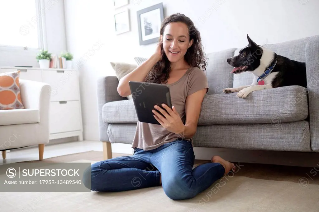 Young woman in living room using digital tablet with her dog