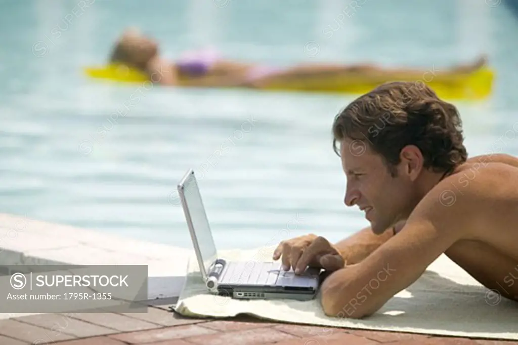A man poolside using a laptop computer