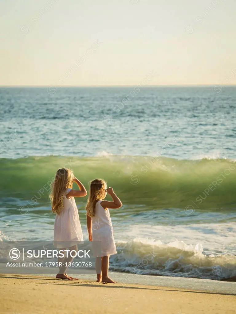 Girls (4-5, 6-7) standing on beach and looking at sea
