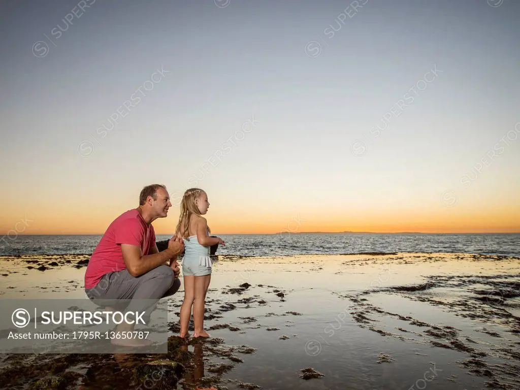 Father crouching next to daughter (4-5) on beach