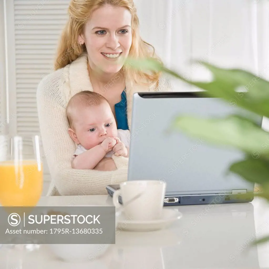 Mother holding baby and using laptop