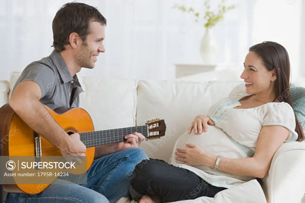 Hispanic man playing guitar for pregnant wife