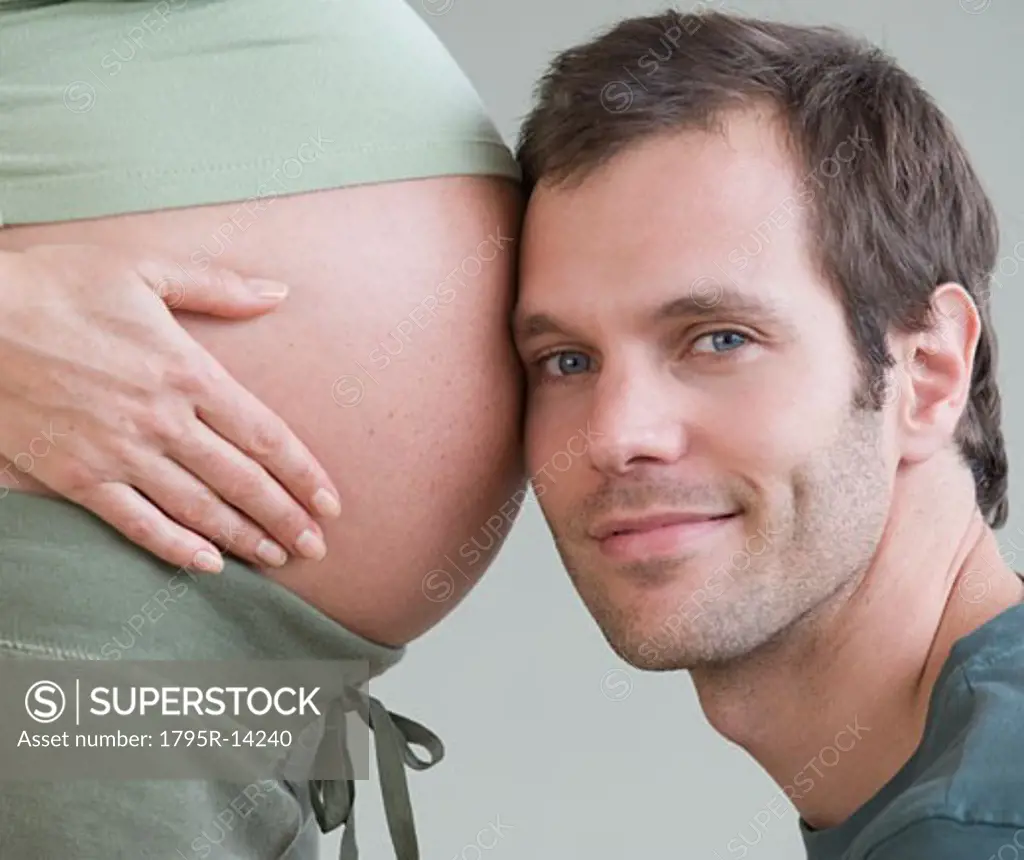 Hispanic man resting head on pregnant wife's belly