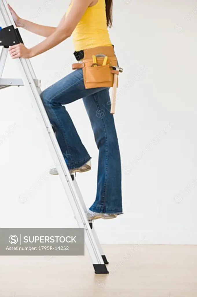 Woman wearing tool belt climbing ladder