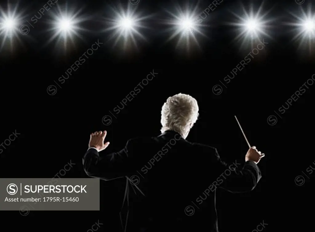Man in tuxedo conducting under lights