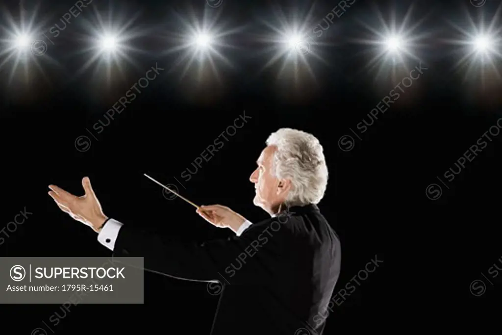 Man in tuxedo conducting under lights