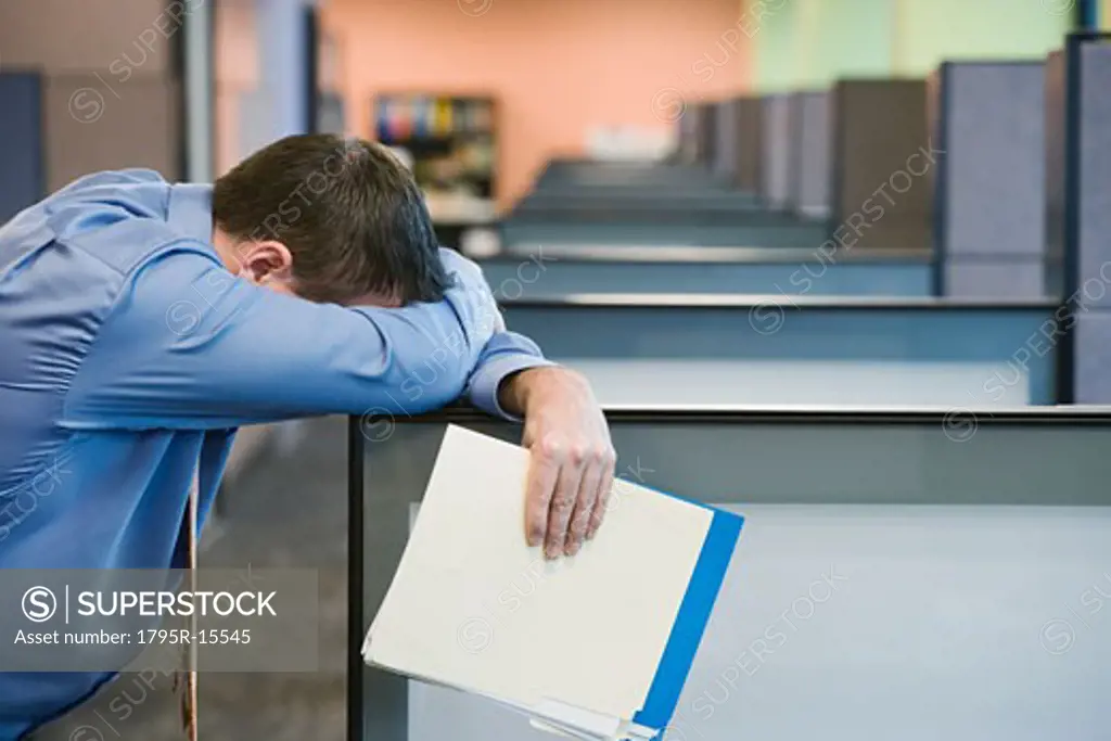 Businessman leaning head on cubicle wall