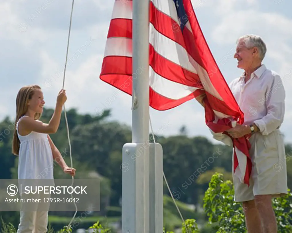 Grandfather and granddaughter raising American flag