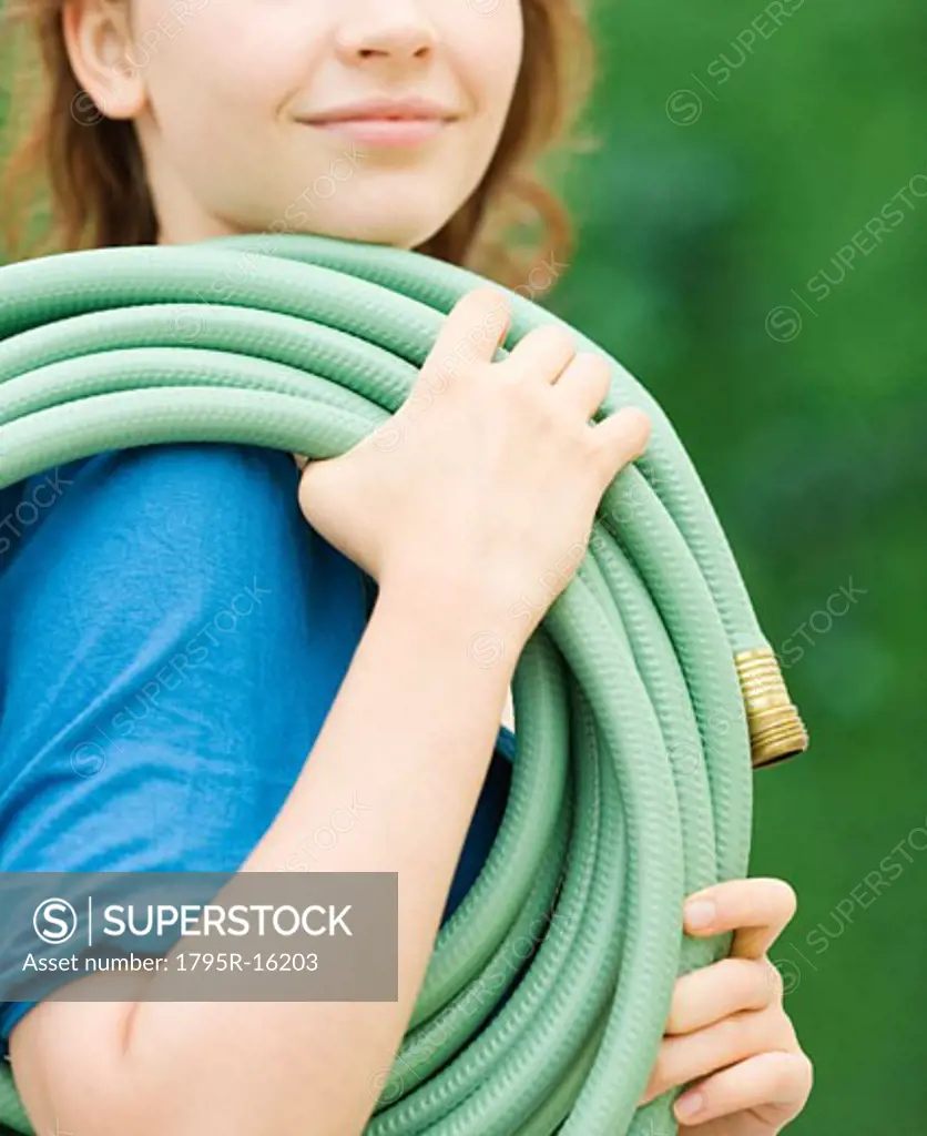 Teenage girl carrying garden hose