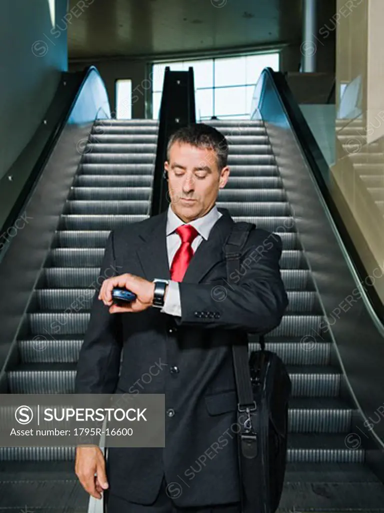 Businessman on escalator checking wristwatch
