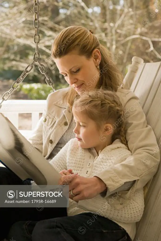Mother reading to daughter on porch swing