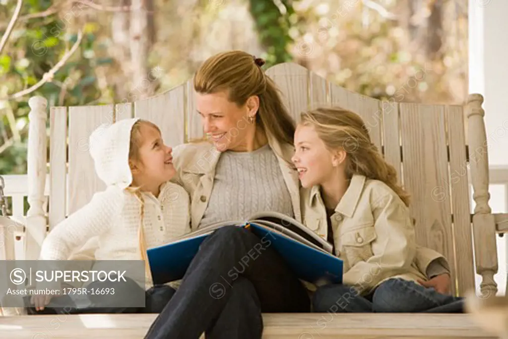 Mother reading to daughters on porch swing