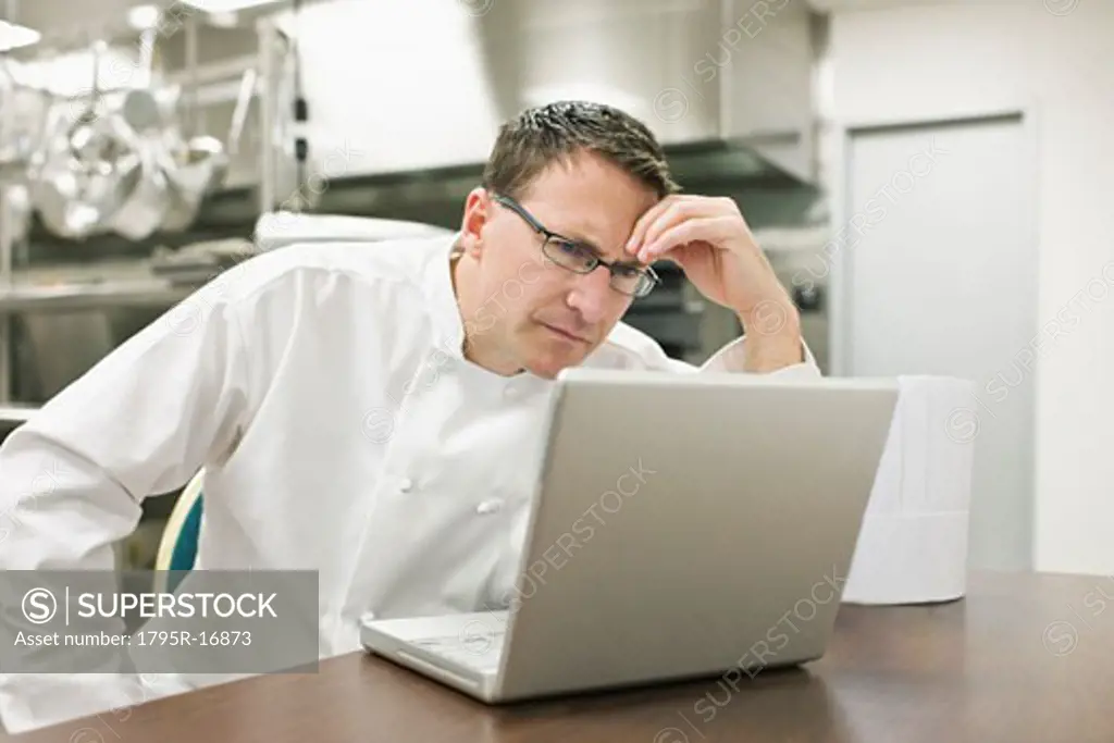 Frustrated chef looking at laptop in kitchen