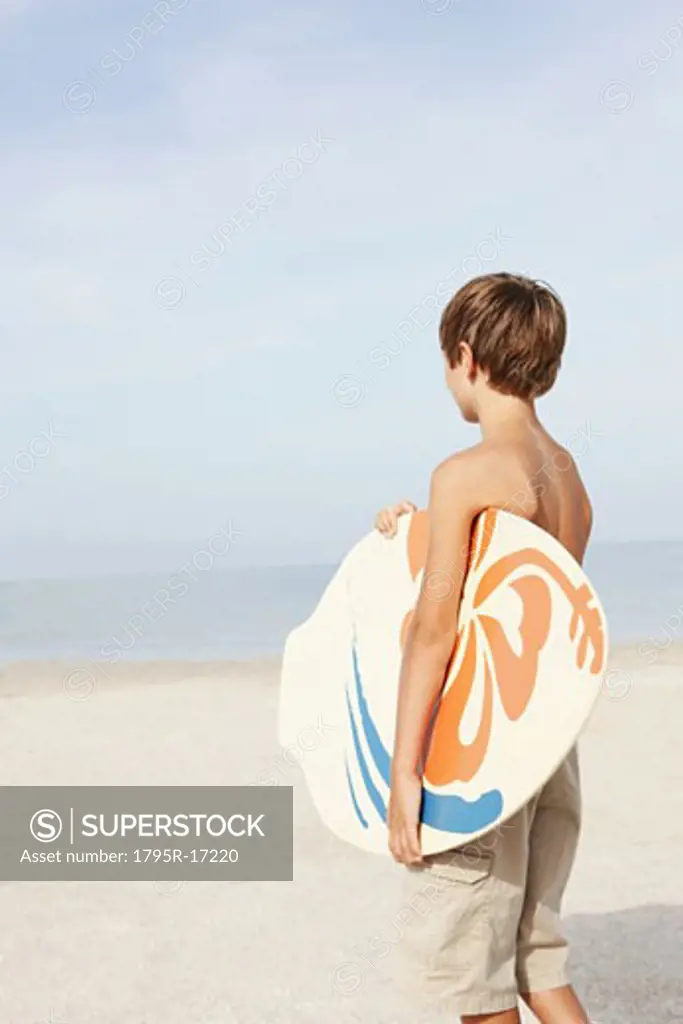 Boy holding skimboard on beach