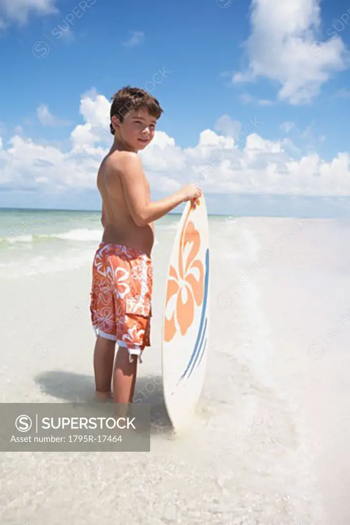 Boy holding skimboard in ocean