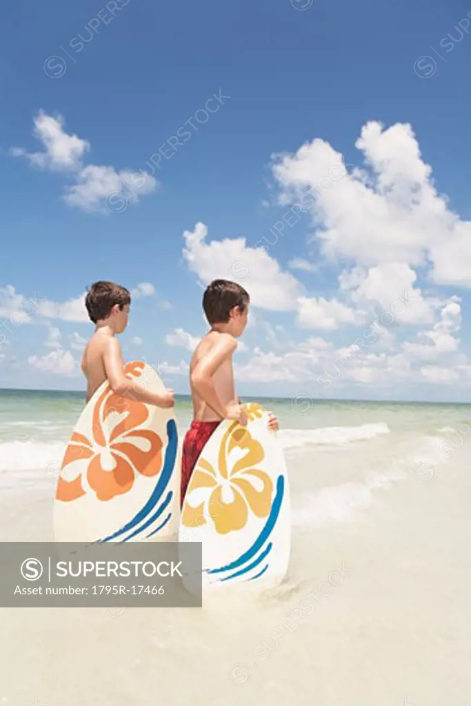 Boys holding skimboards in ocean