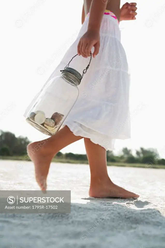 Girl on beach carrying jar of shells