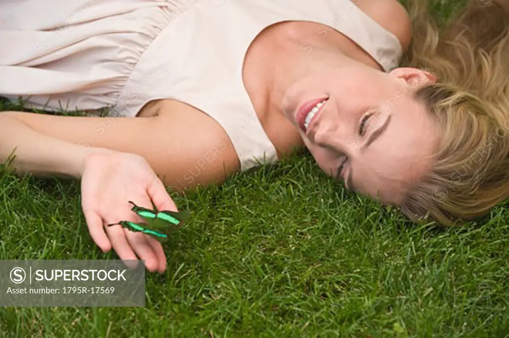 Woman laying on grass holding green butterfly