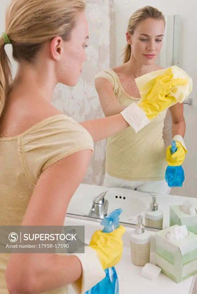 Woman cleaning mirror in bathroom