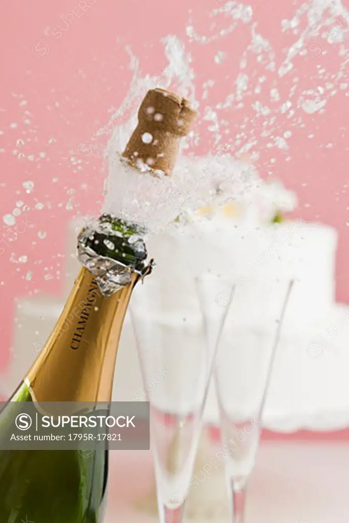 Cork exploding from champagne bottle with wedding cake in background