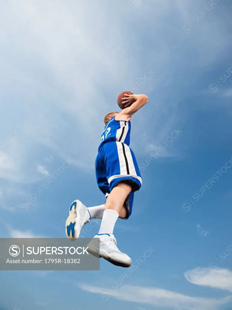 Teenage basketball player in mid-air shooting basketball