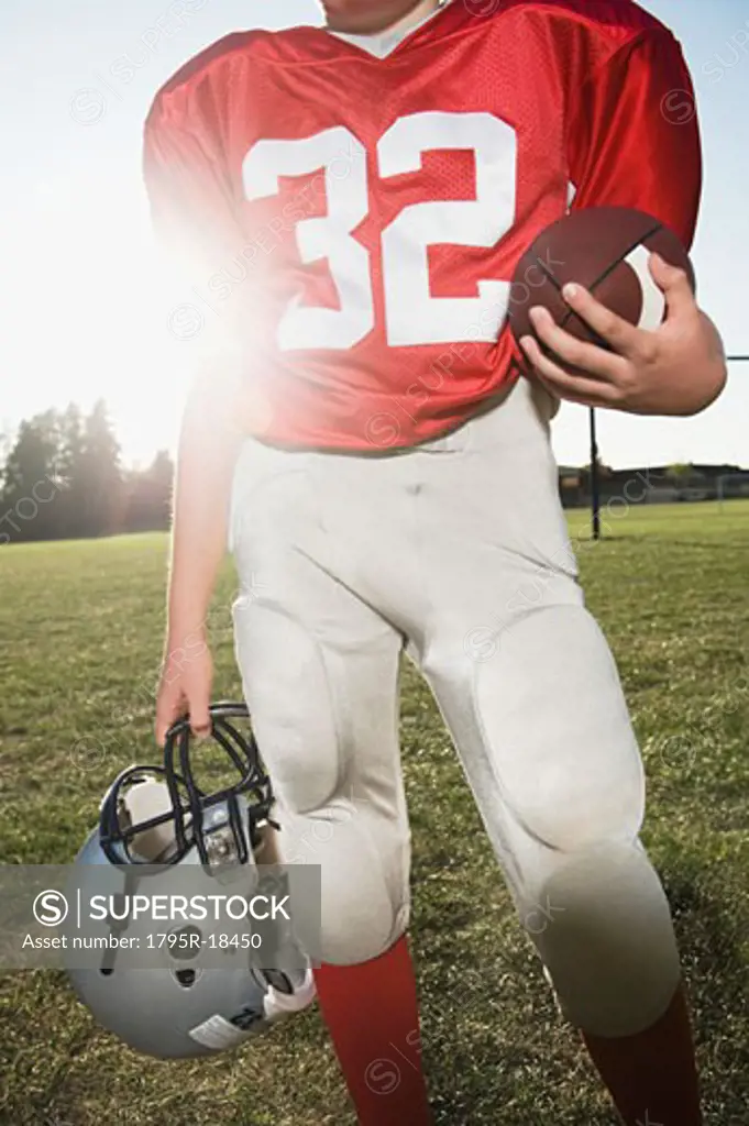 Football player holding helmet and football on field