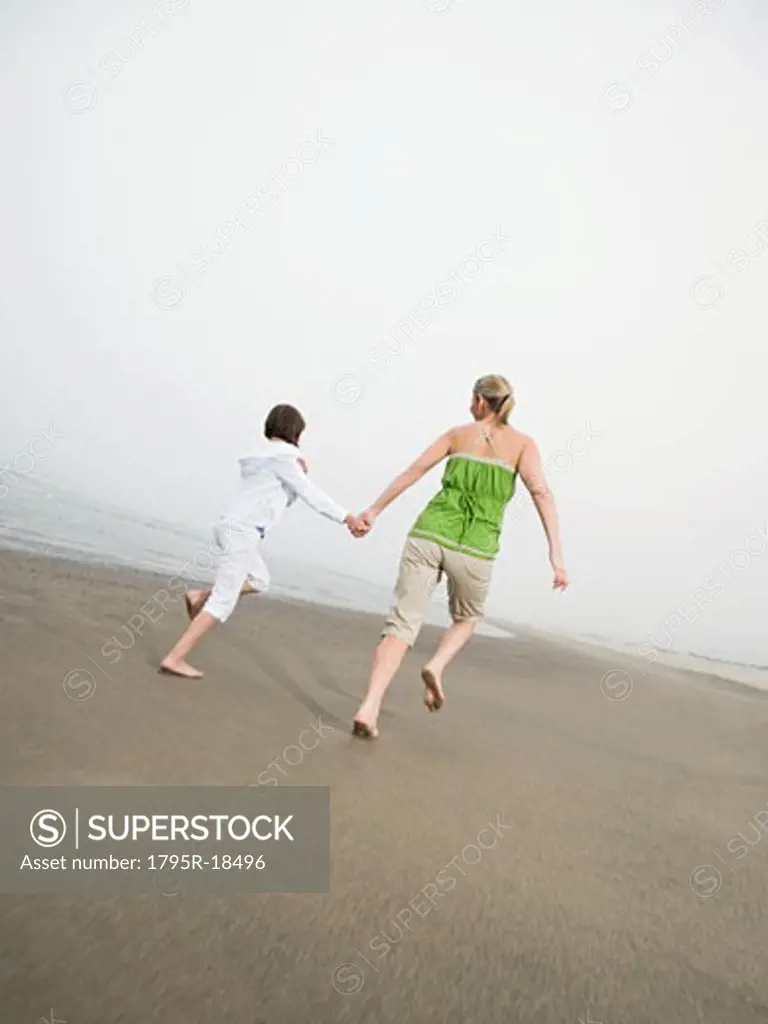 Mother and daughter holding hands and running on beach