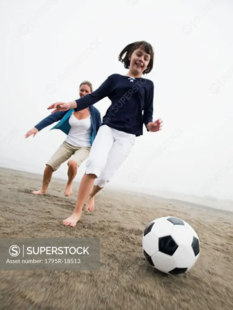 Mother and daughter playing soccer on beach