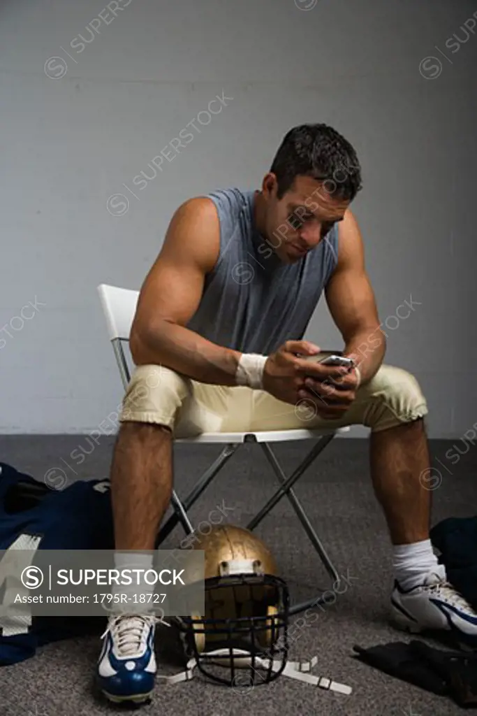 Football player looking at cell phone in locker room