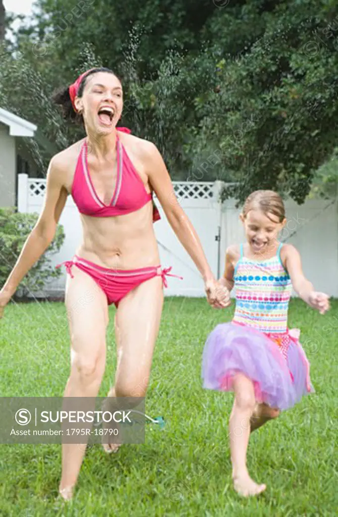Mother and daughter running through sprinkler