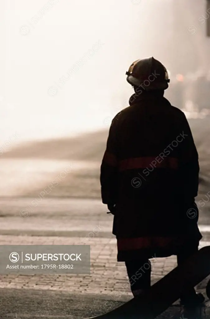 Silhouette of fireman looking at smoke in distance