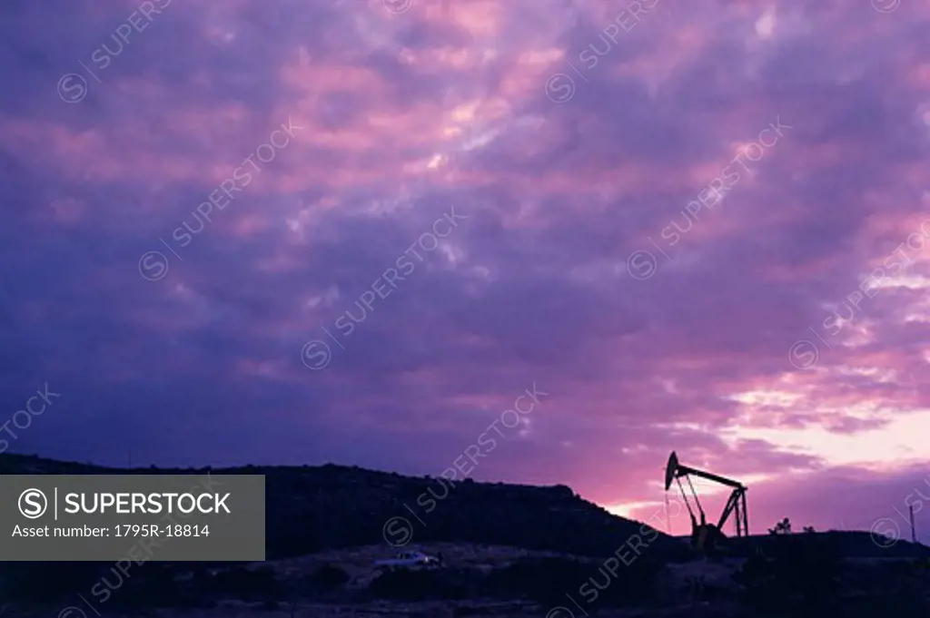 Oil rig in distance under sunset sky