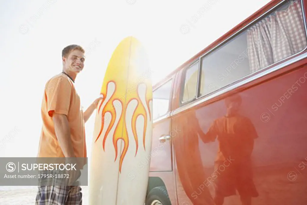 Portrait of young man holding surfboard near van