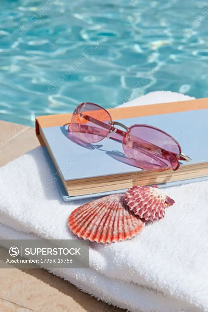 Book and sunglasses by swimming pool