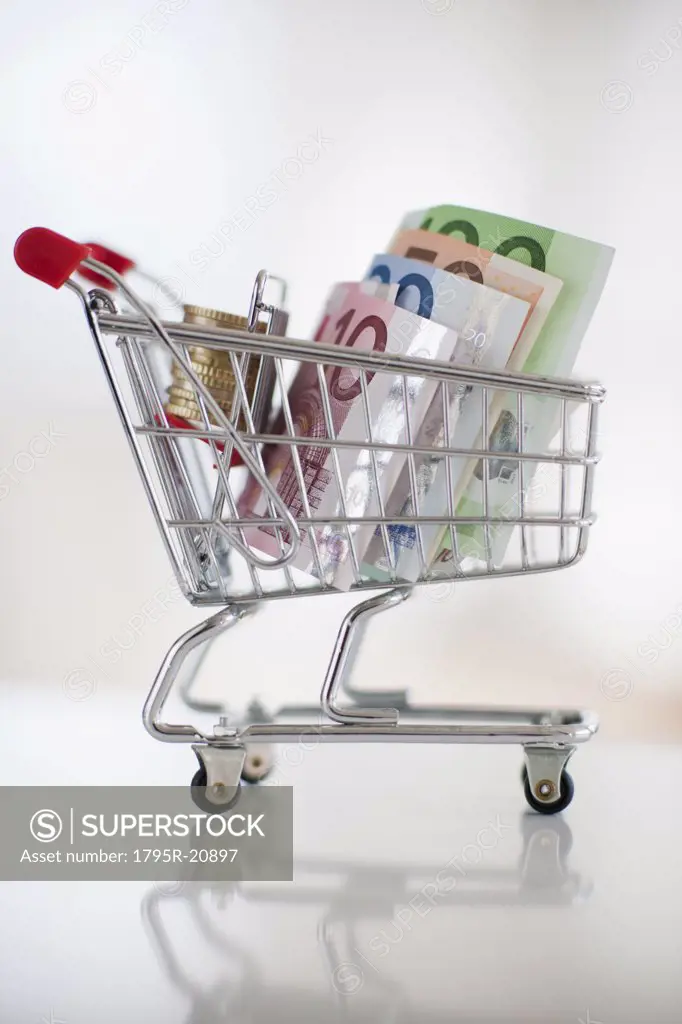 A miniature shopping cart with bank notes and coins