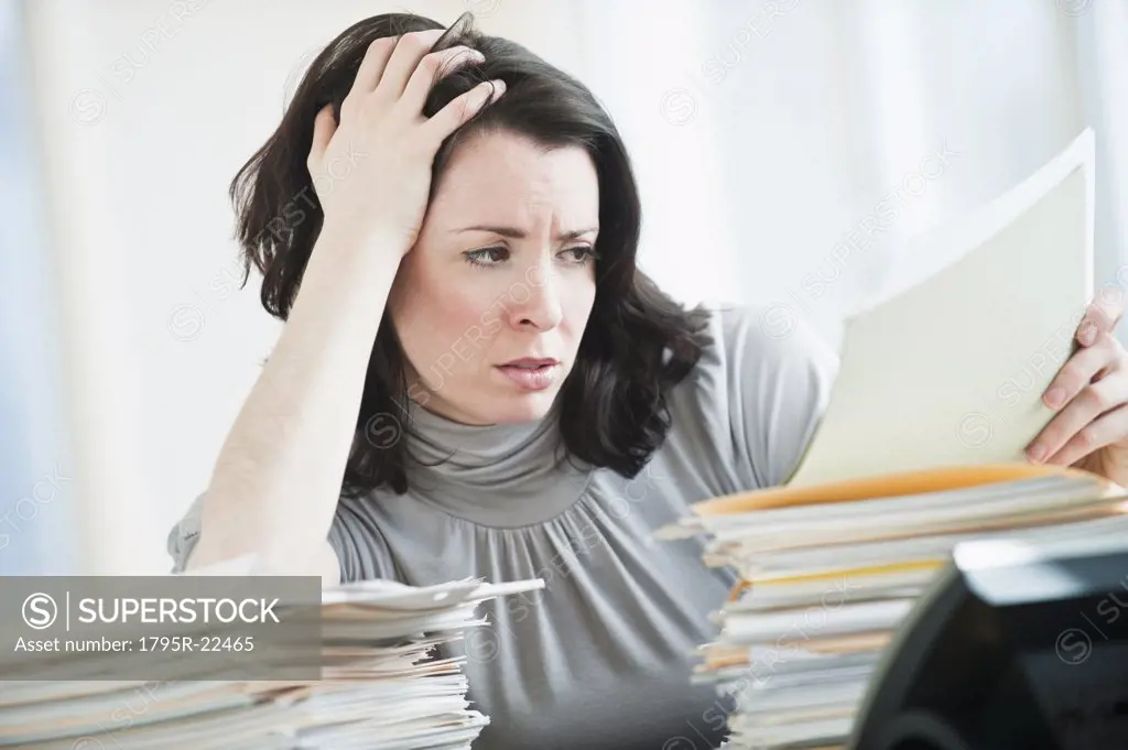 Stressed business woman reading paperwork in office