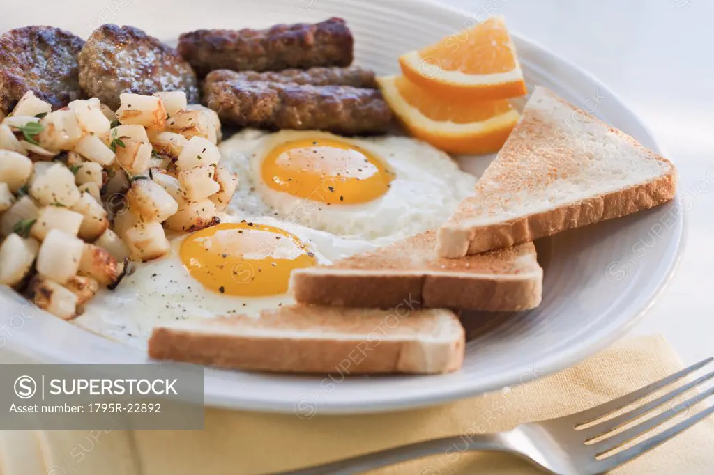 Fried sausages on plate with eggs and plates in background