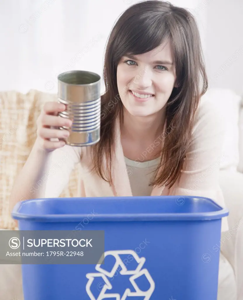 Portrait of young woman putting can in recycling bin