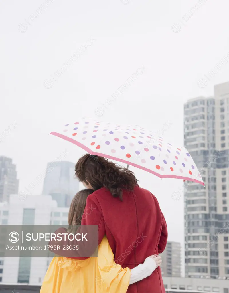 USA, New York City, mother and daughter (10-12 years) embracing under umbrella, rear view, Jersey City, New Jersey