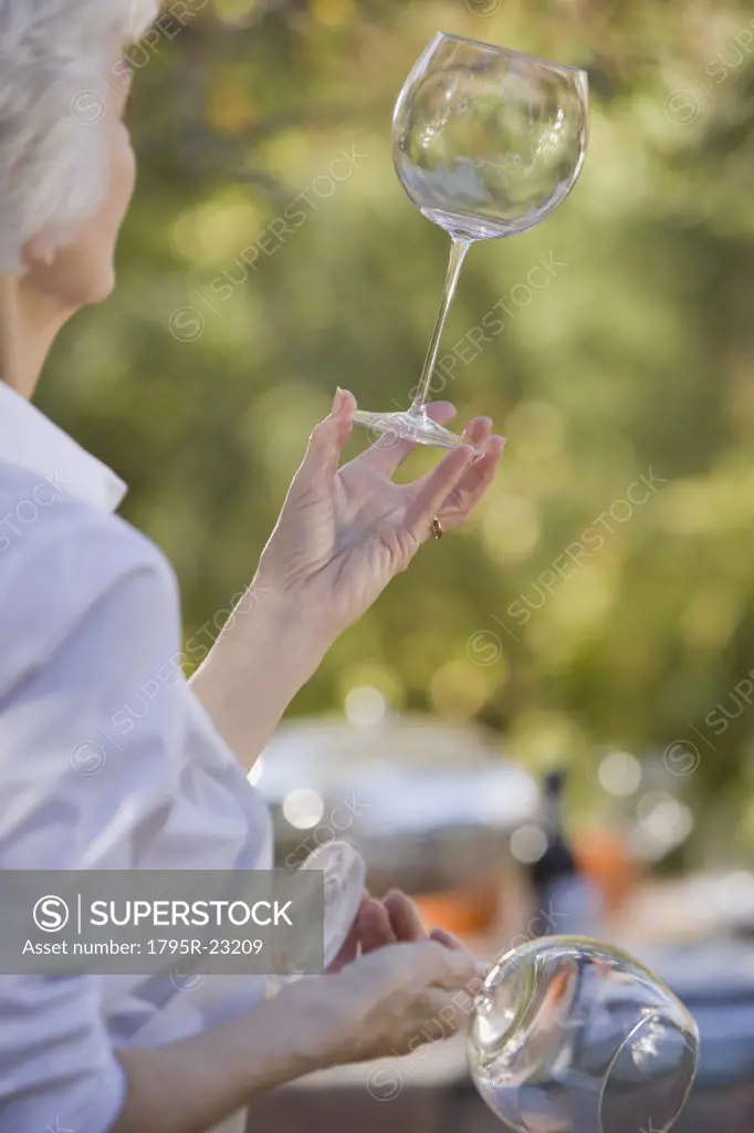 Senior woman standing in garden and examining wineglasses