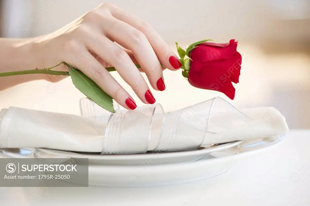 Hand putting a red rose on a place setting
