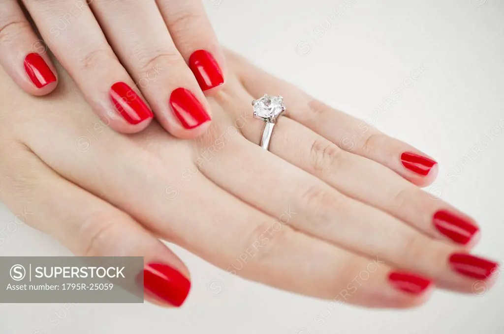 Diamond engagement ring on hands with red nail polish