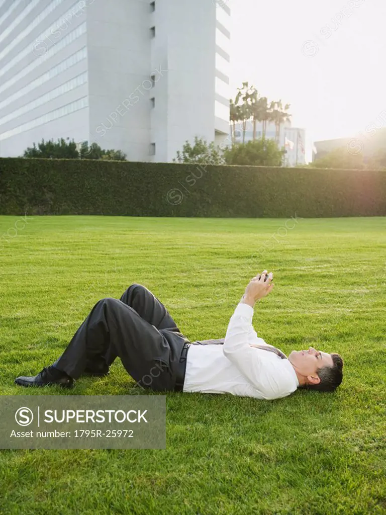 Businessman texting while lying on grass